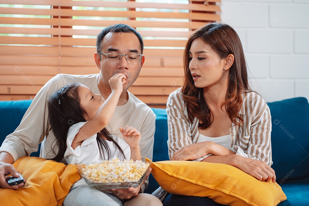 Família asiática composta por pais, filho feliz e filha assistindo TV ou filme juntos no sofá na sala de estar em casa.
