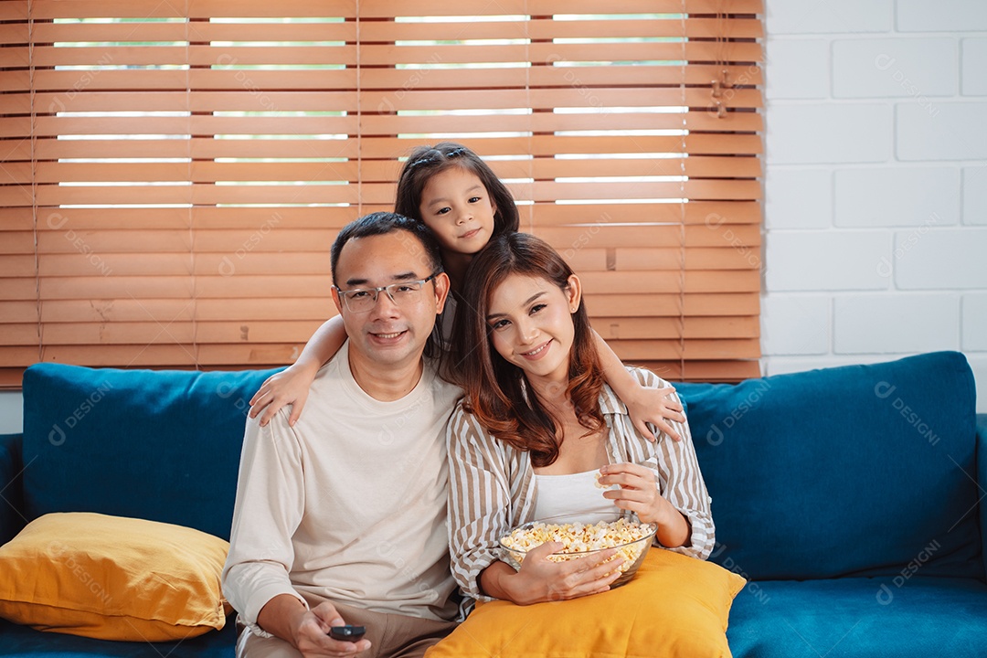 Família asiática composta por pais, filha feliz assistindo TV ou filme comendo pipoca