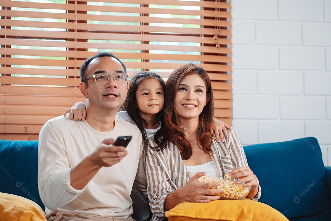 Família asiática composta por pais, filha feliz assistindo TV ou filme comendo pipoca