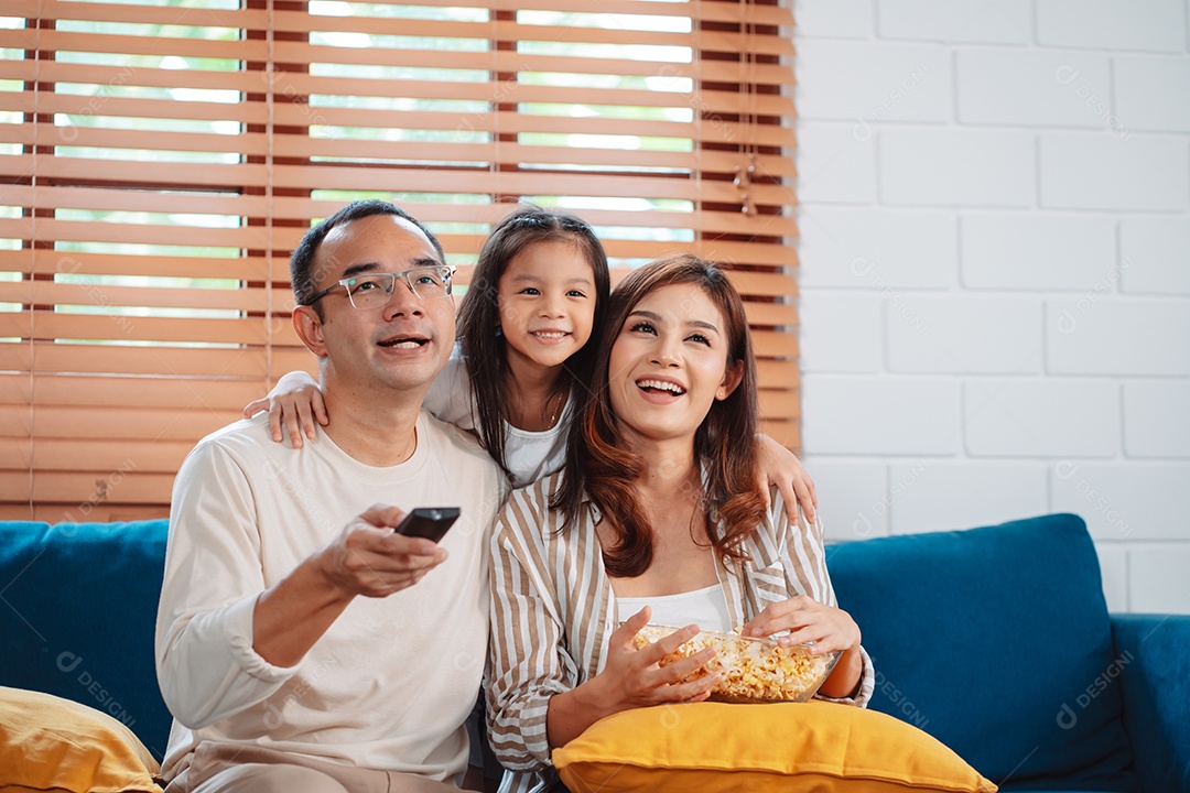 Família asiática composta por pais, filha feliz assistindo TV ou filme comendo pipoca