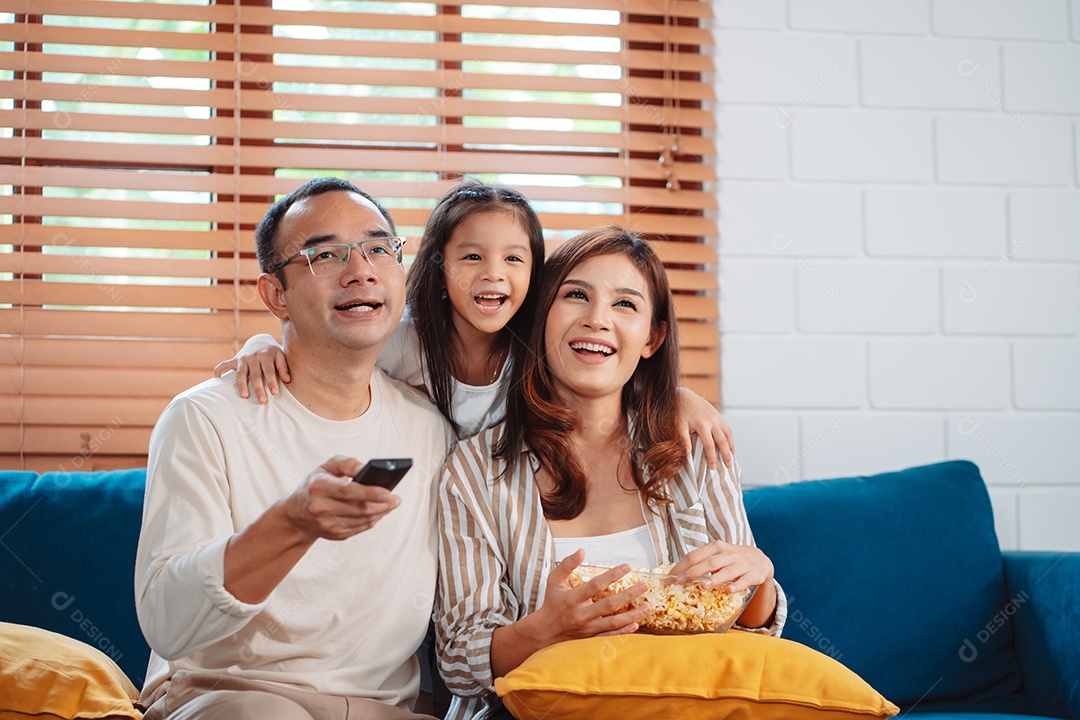 Família asiática composta por pais, filha feliz assistindo TV ou filme comendo pipoca