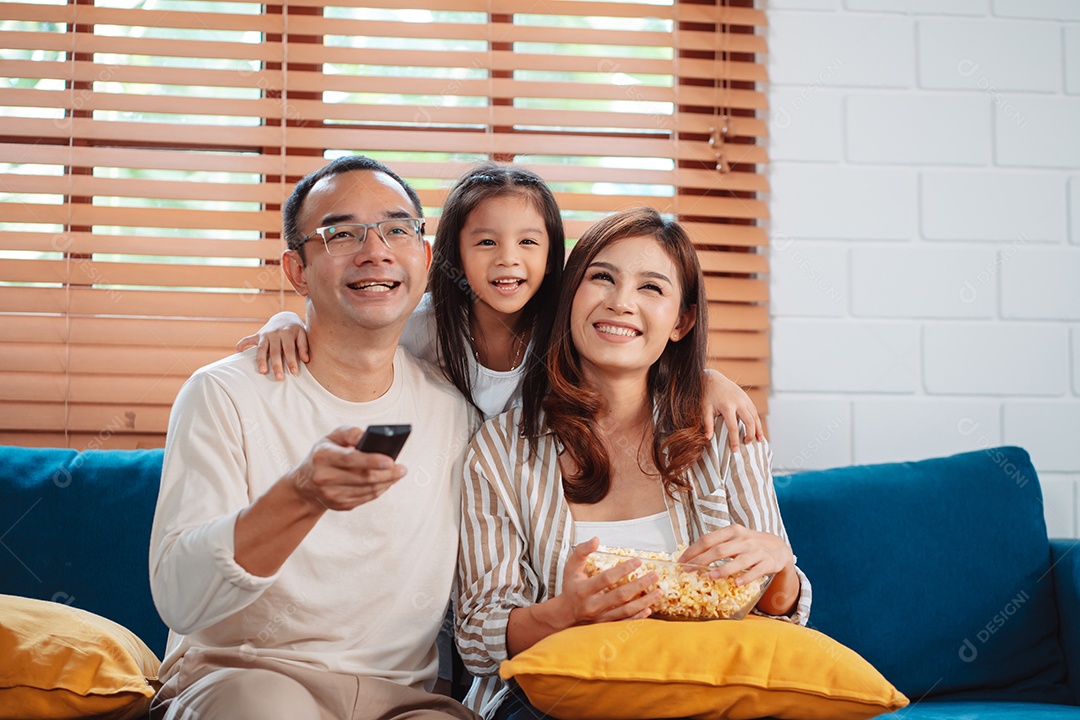 Família asiática composta por pais, filha feliz assistindo TV ou filme comendo pipoca