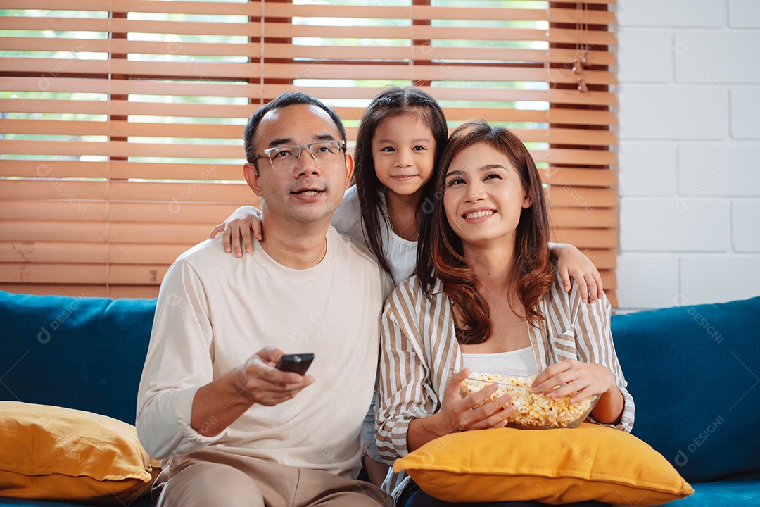 Família asiática composta por pais, filha feliz assistindo TV ou filme comendo pipoca
