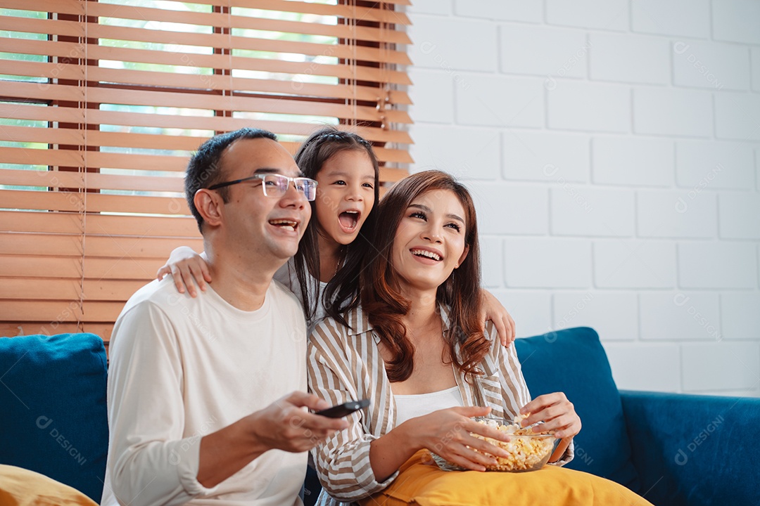 Família asiática composta por pais, filha feliz assistindo TV ou filme comendo pipoca