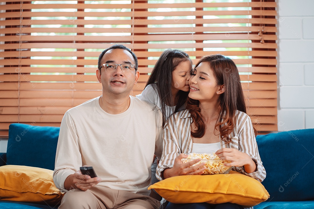 Família asiática composta por pais, filha feliz assistindo TV ou filme comendo pipoca