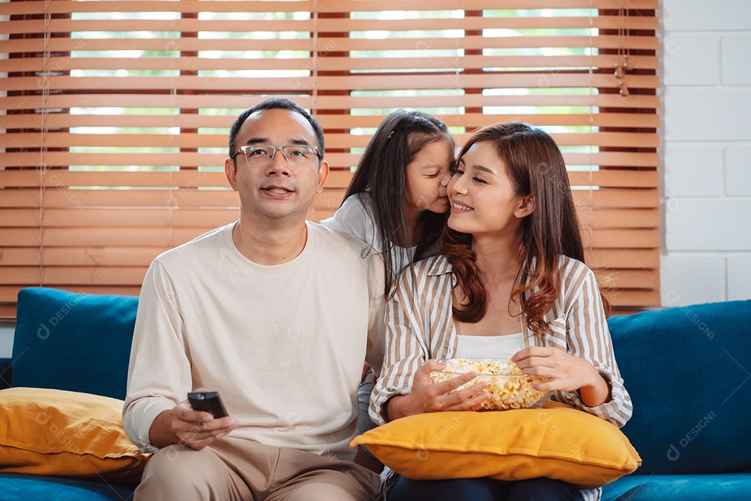 Família asiática composta por pais, filha feliz assistindo TV ou filme comendo pipoca