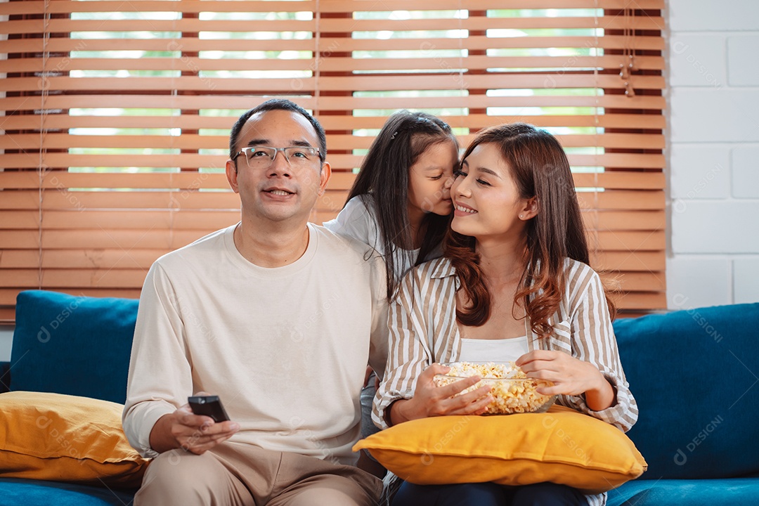 Família asiática composta por pais, filha feliz assistindo TV ou filme comendo pipoca