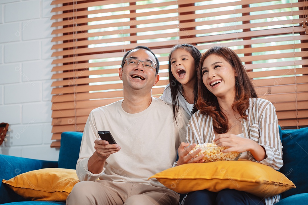Família asiática composta por pais, filha feliz assistindo TV ou filme comendo pipoca