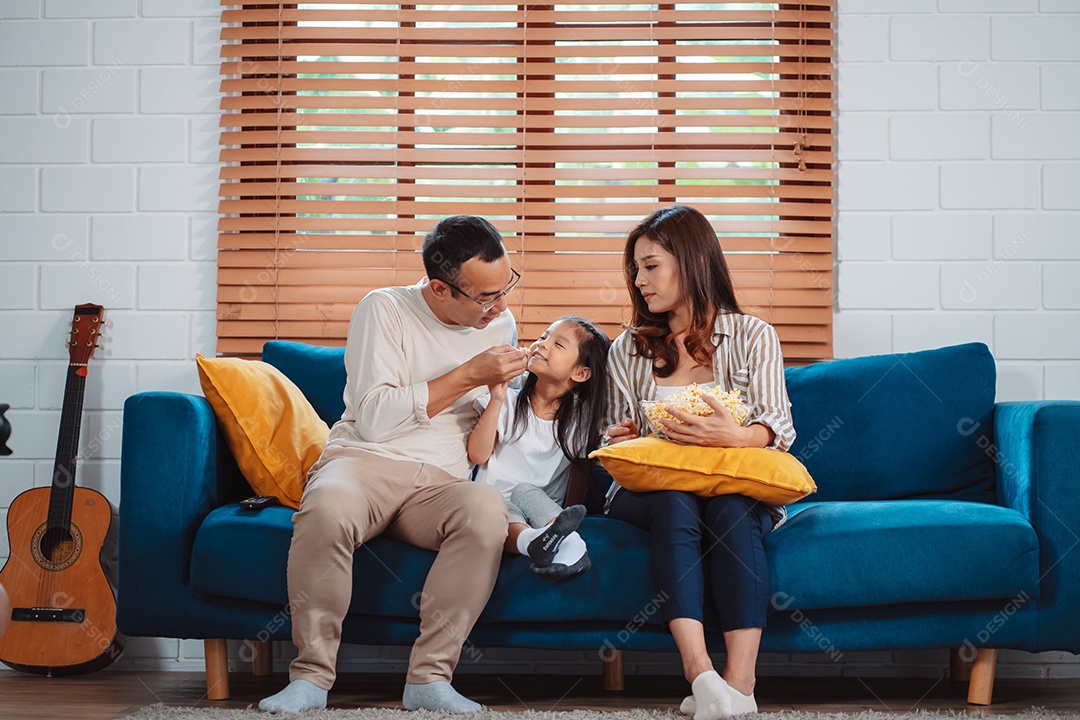 Família asiática composta por pais, filha feliz assistindo TV ou filme comendo pipoca
