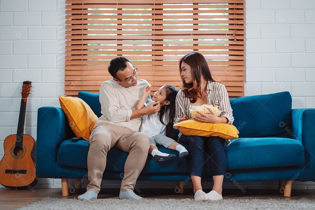 Família asiática composta por pais, filha feliz assistindo TV ou filme comendo pipoca