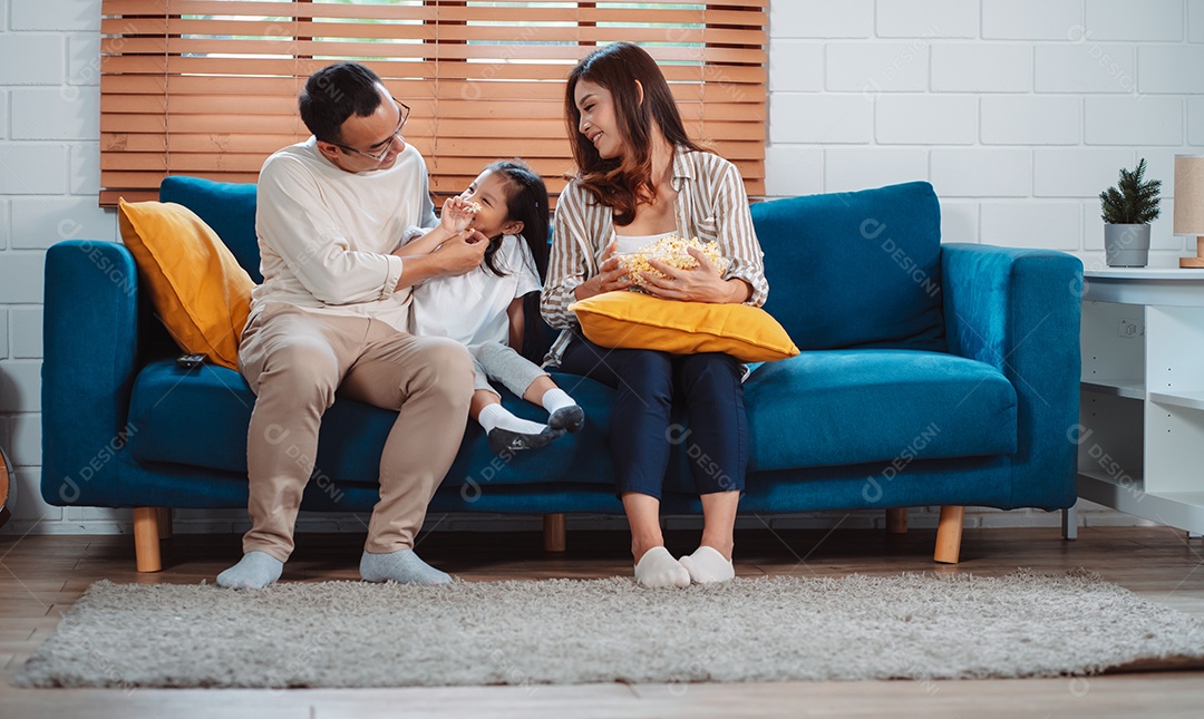 Família asiática composta por pais, filha feliz assistindo TV ou filme comendo pipoca