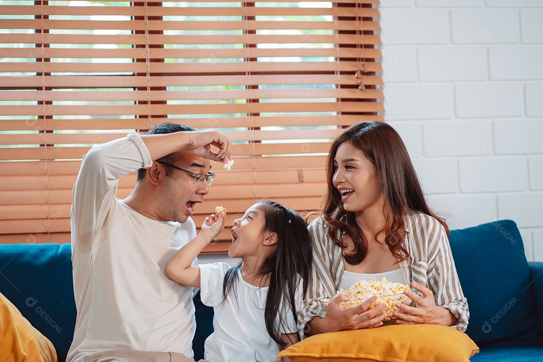 Família asiática composta por pais, filha feliz assistindo TV ou filme comendo pipoca