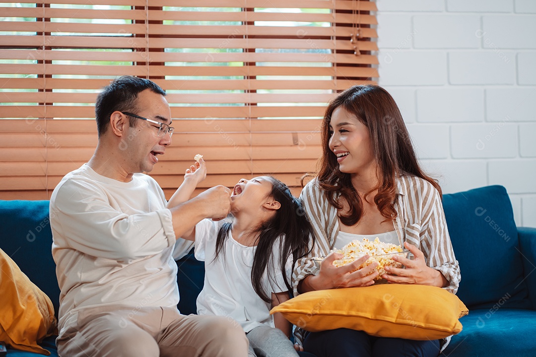 Família asiática composta por pais, filha feliz assistindo TV ou filme comendo pipoca