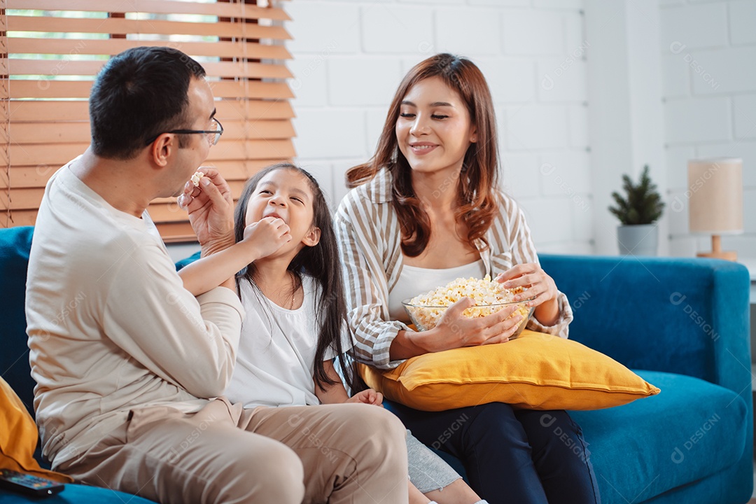 Família asiática composta por pais, filha feliz assistindo TV ou filme comendo pipoca