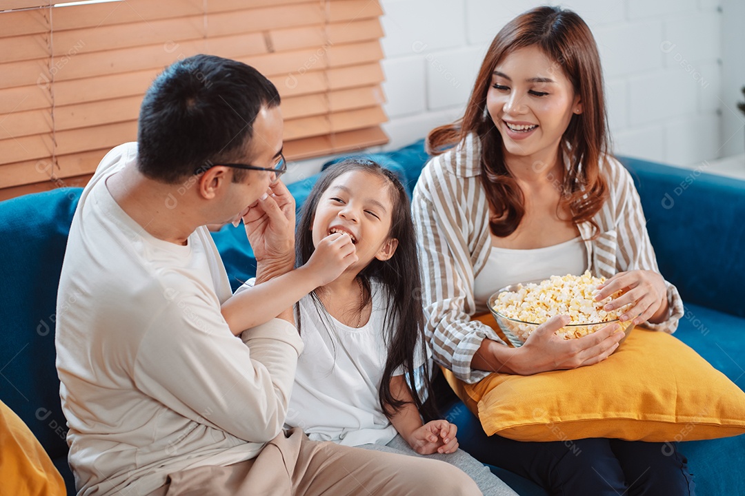 Família asiática composta por pais, filha feliz assistindo TV ou filme comendo pipoca