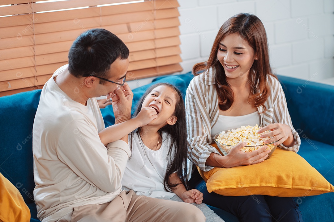 Família asiática composta por pais, filha feliz assistindo TV ou filme comendo pipoca