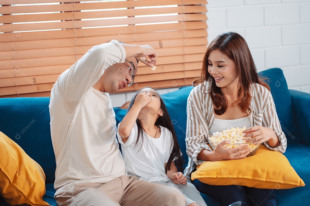 Família asiática composta por pais, filha feliz assistindo TV ou filme comendo pipoca