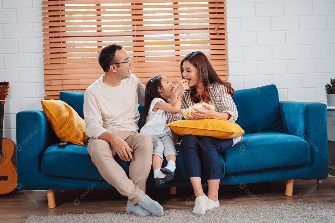 Família asiática composta por pais, filha feliz assistindo TV ou filme comendo pipoca