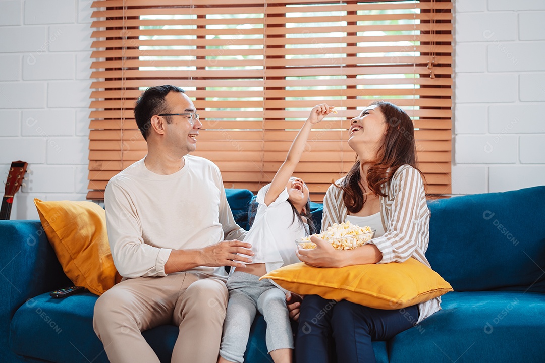 Família asiática composta por pais, filha feliz assistindo TV ou filme comendo pipoca