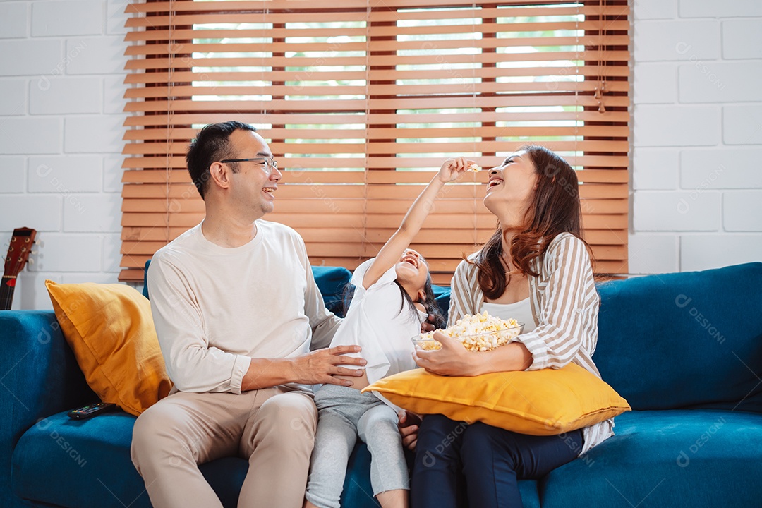 Família asiática composta por pais, filha feliz assistindo TV ou filme comendo pipoca