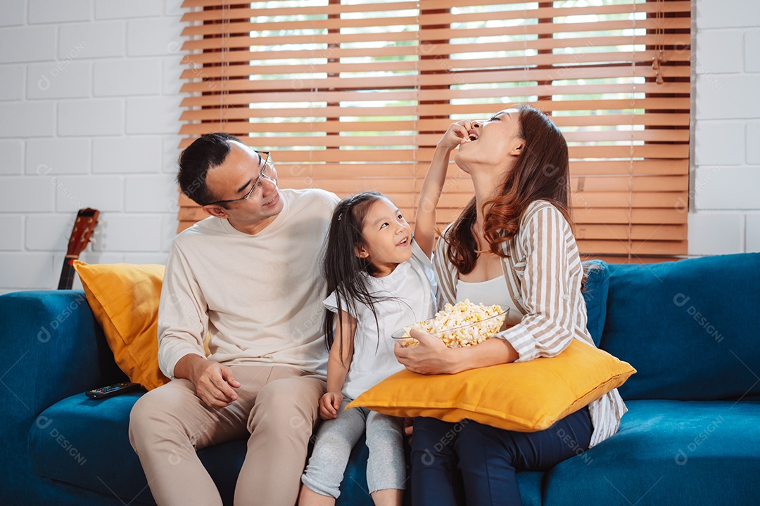 Família asiática composta por pais, filha feliz assistindo TV ou filme comendo pipoca