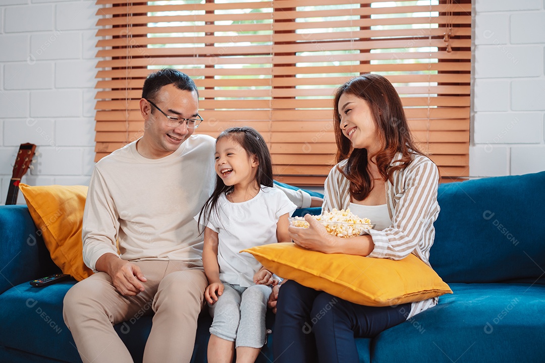 Família asiática composta por pais, filha feliz assistindo TV ou filme comendo pipoca