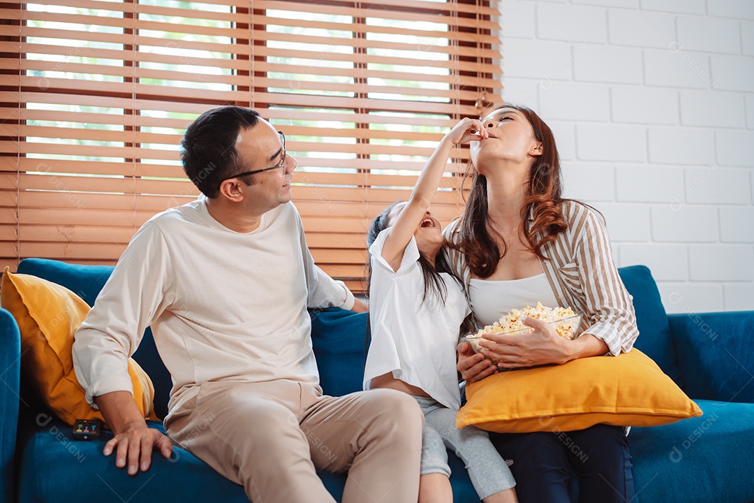 Família asiática composta por pais, filha feliz assistindo TV ou filme comendo pipoca