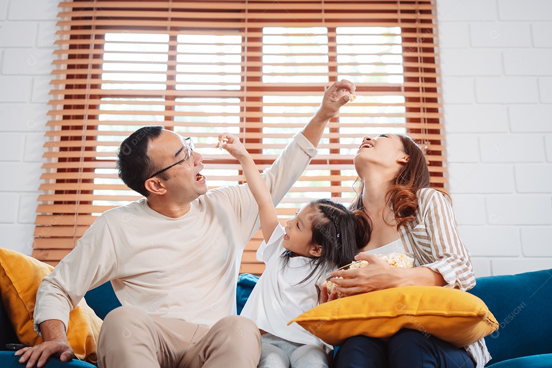 Família asiática composta por pais, filha feliz assistindo TV ou filme comendo pipoca