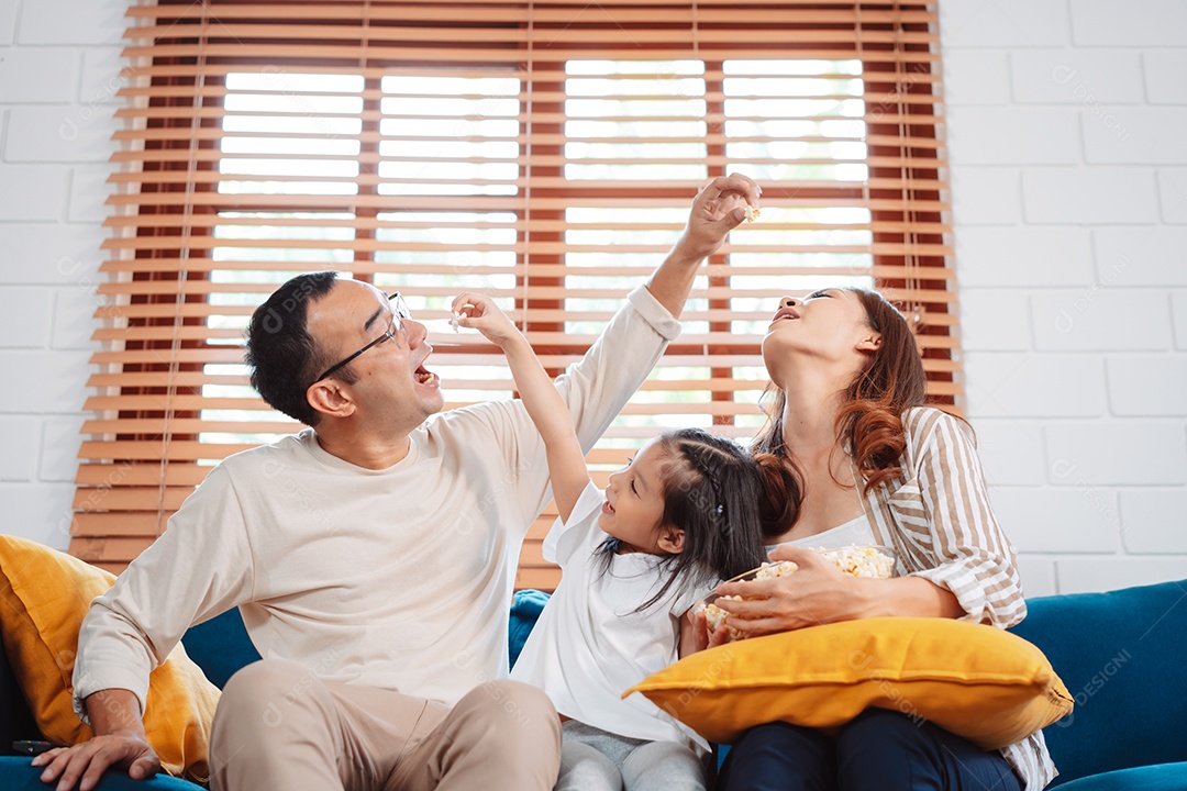 Família asiática composta por pais, filha feliz assistindo TV ou filme comendo pipoca