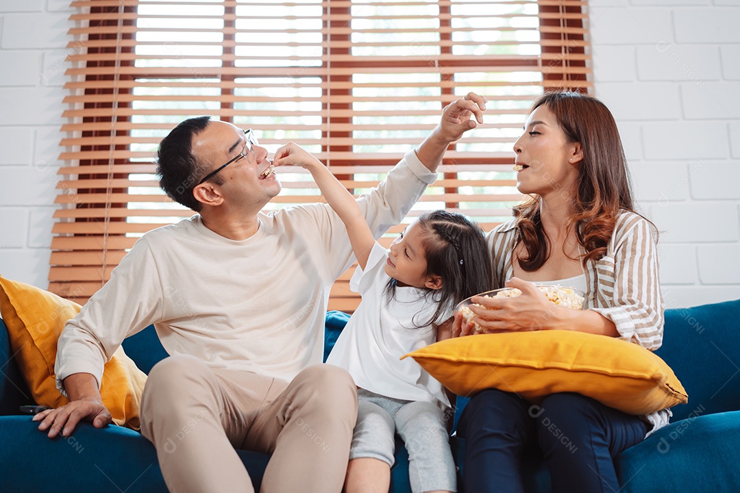 Família asiática composta por pais, filha feliz assistindo TV ou filme comendo pipoca