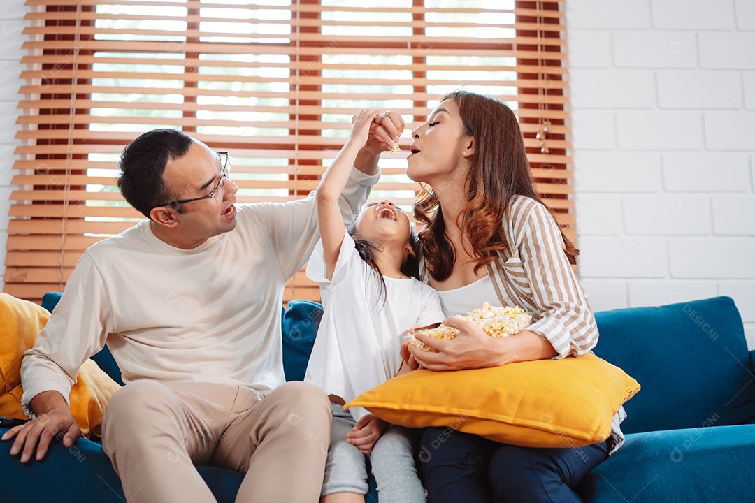Família asiática composta por pais, filha feliz assistindo TV ou filme comendo pipoca