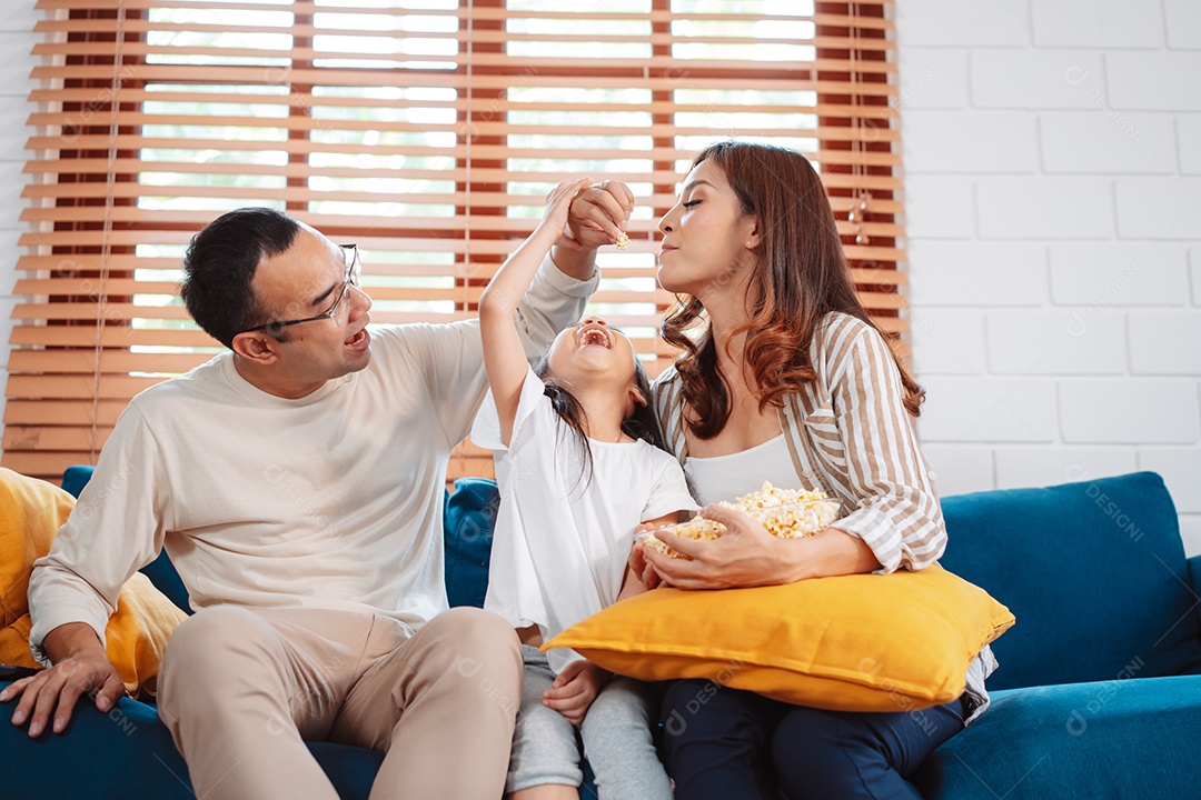 Família asiática composta por pais, filha feliz assistindo TV ou filme comendo pipoca