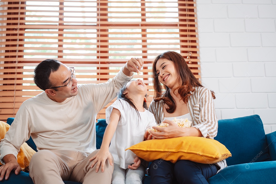 Família asiática composta por pais, filha feliz assistindo TV ou filme comendo pipoca