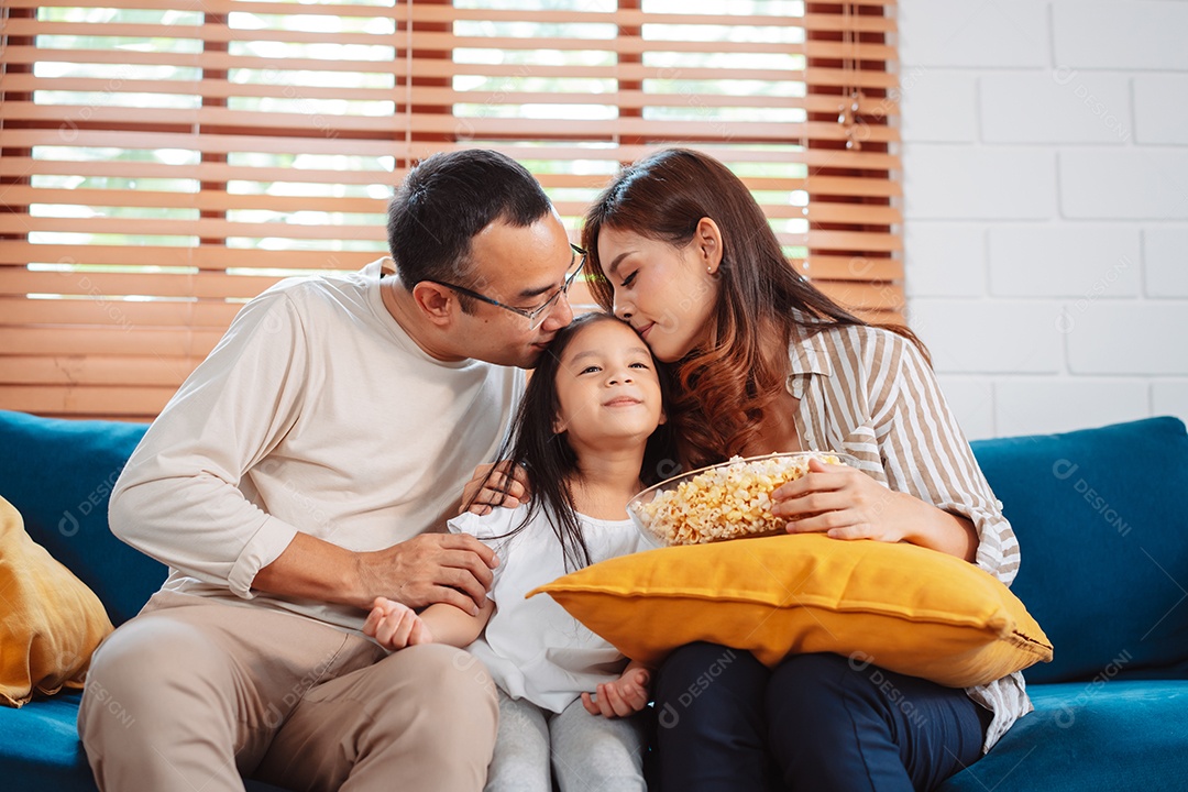 Família asiática composta por pais, filha feliz assistindo TV ou filme comendo pipoca