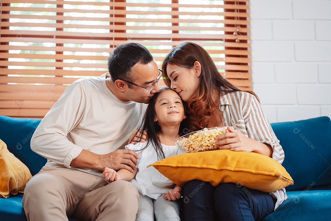 Família asiática composta por pais, filha feliz assistindo TV ou filme comendo pipoca