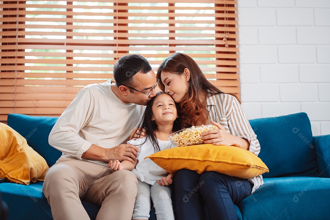 Família asiática composta por pais, filha feliz assistindo TV ou filme comendo pipoca