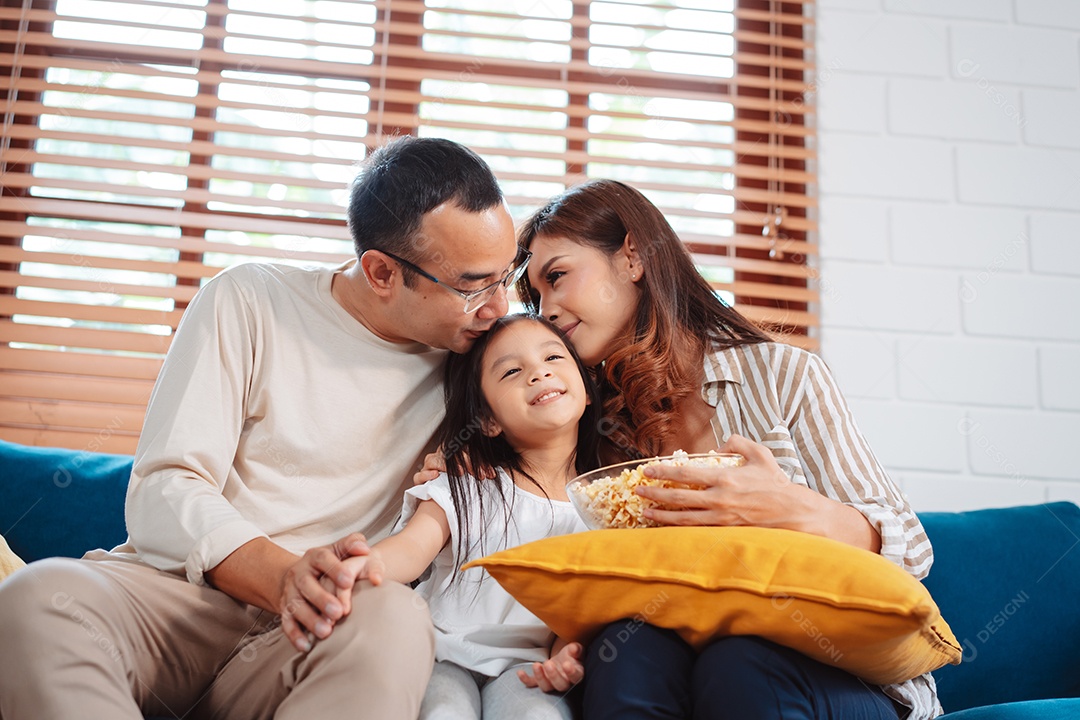 Família asiática composta por pais, filha feliz assistindo TV ou filme comendo pipoca