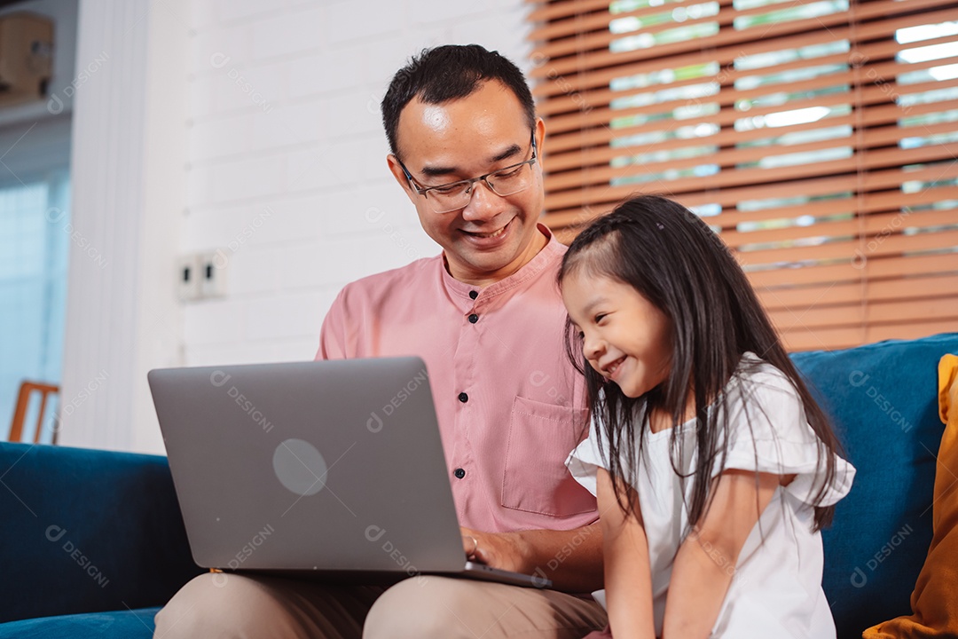 Filha asiática bonitinha com o pai trabalhando no laptop em casa.