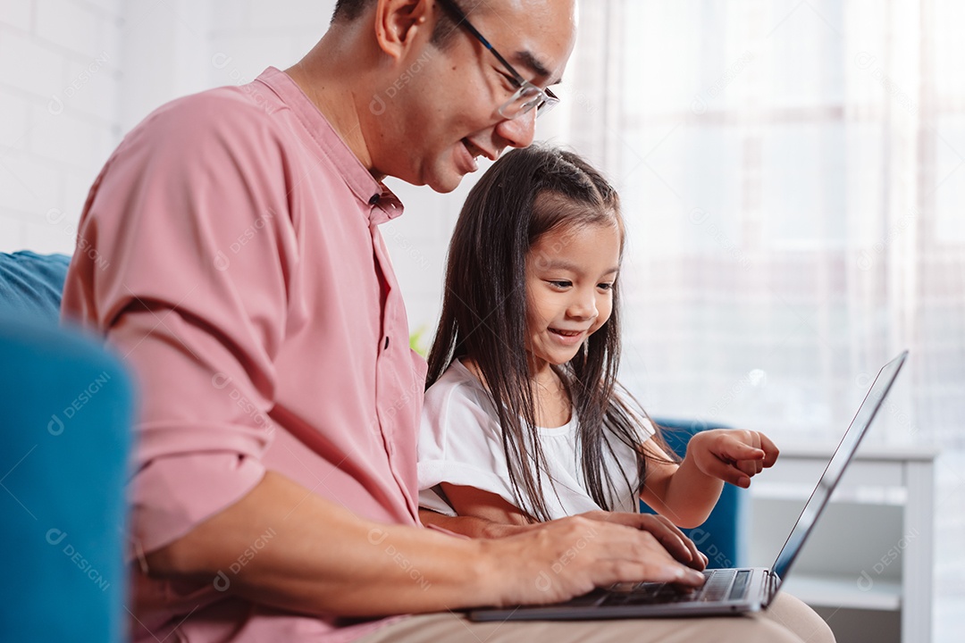 Filha asiática bonitinha com o pai trabalhando no laptop em casa.