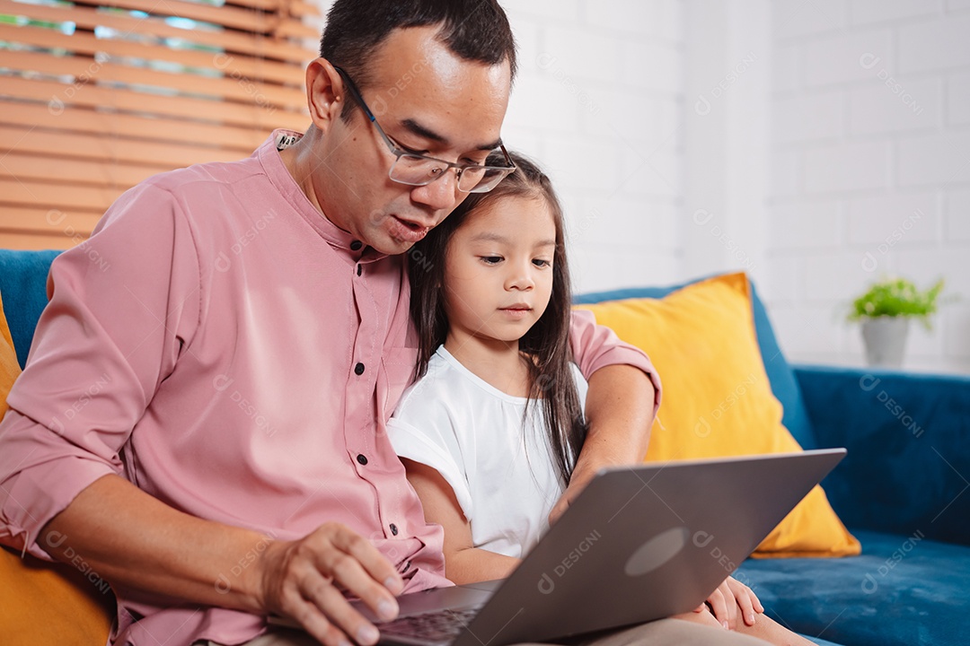 Filha asiática bonitinha com o pai trabalhando no laptop em casa.