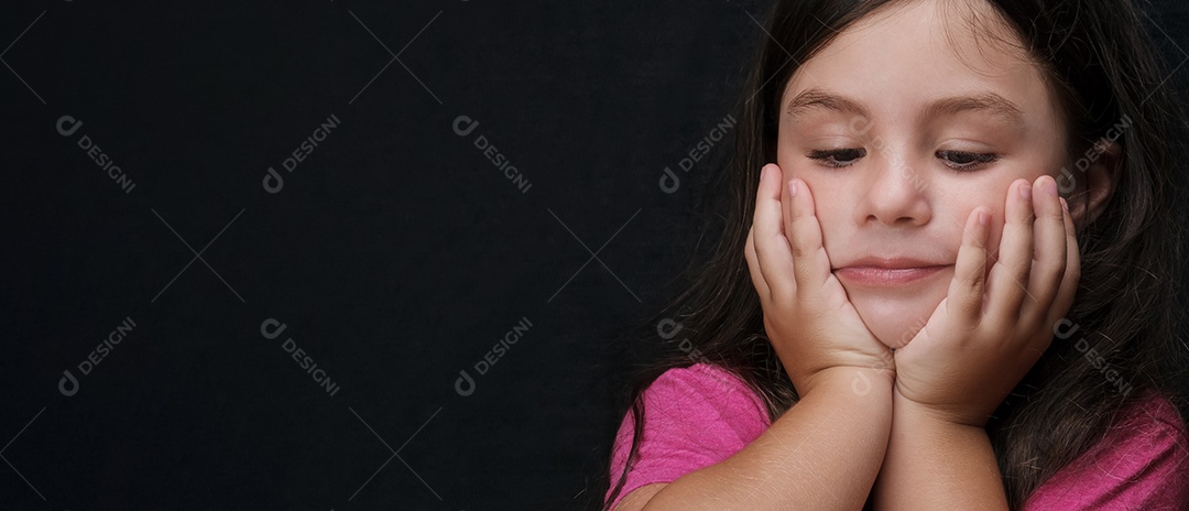 Retrato de uma menina pensativa com as mãos apoiando o queixo e olhando para baixo