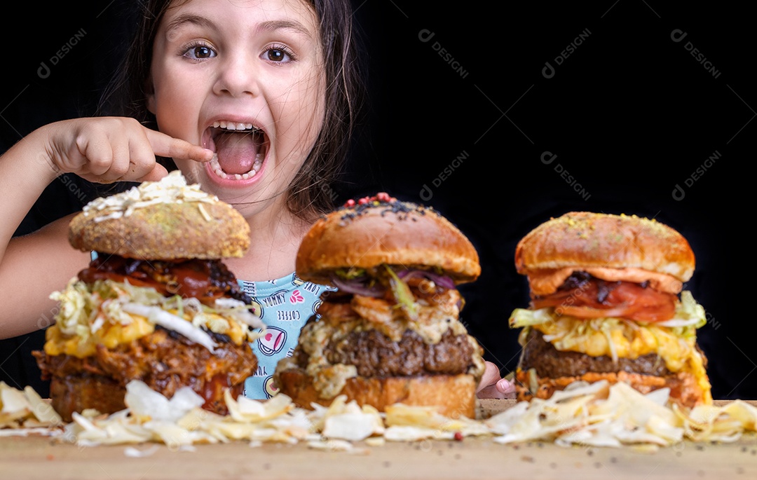 Adorável menina com boca aberta e expressão feliz pronta para comer três hambúrgueres