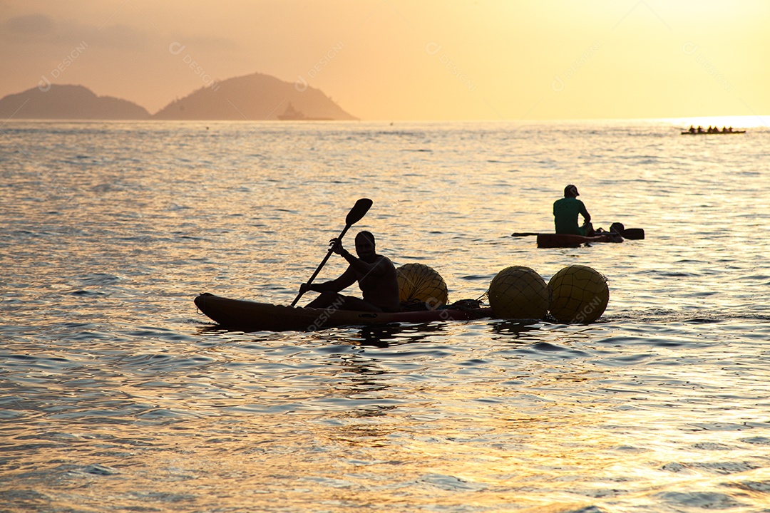 silhuetas de pessoas em canoas ao amanhecer na praia de Copacabana, no Rio de Janeiro