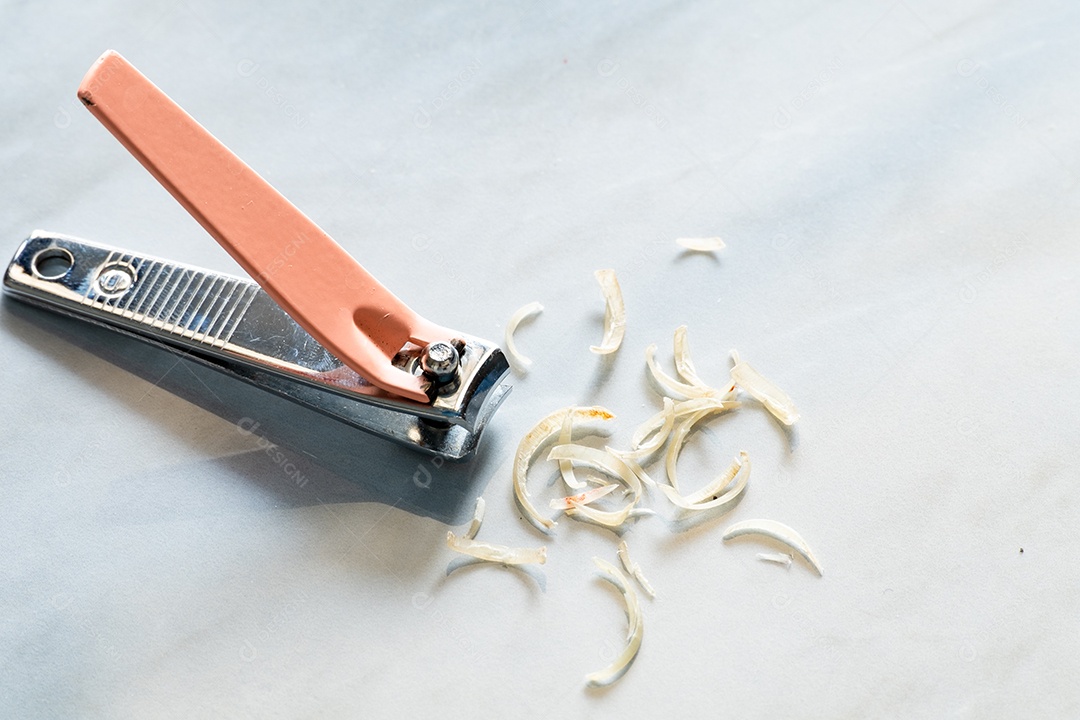 Cortador de unhas rosa é colocado perto de uma unha cortada em um piso de cerâmica na casa