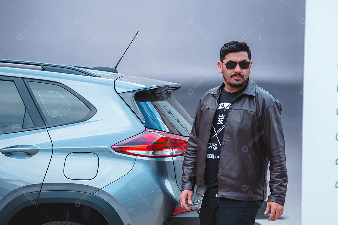 Homem lindo de jaqueta e usando óculos andando ao lado de uma carro