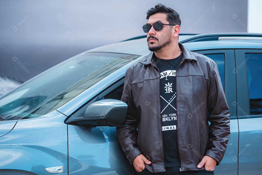 Homem lindo de jaqueta e usando óculos ao lado de uma carro