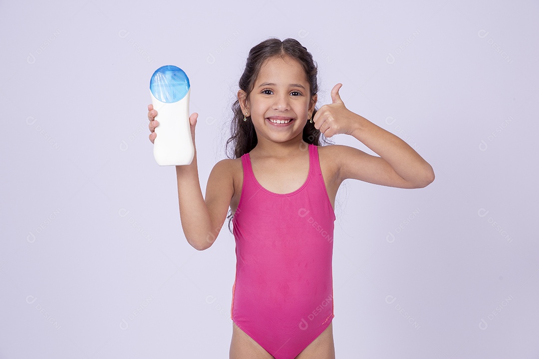 Linda garotinha sorridente com maiô segurando frasco de protetor solar