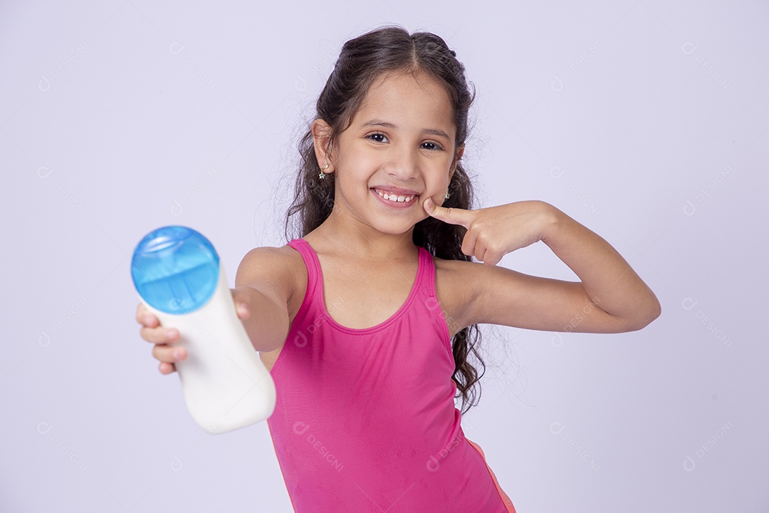 Linda garotinha sorridente com maiô segurando frasco de protetor solar