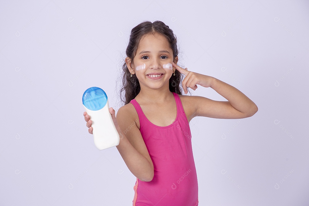 Linda garotinha sorridente com maiô segurando frasco de protetor solar