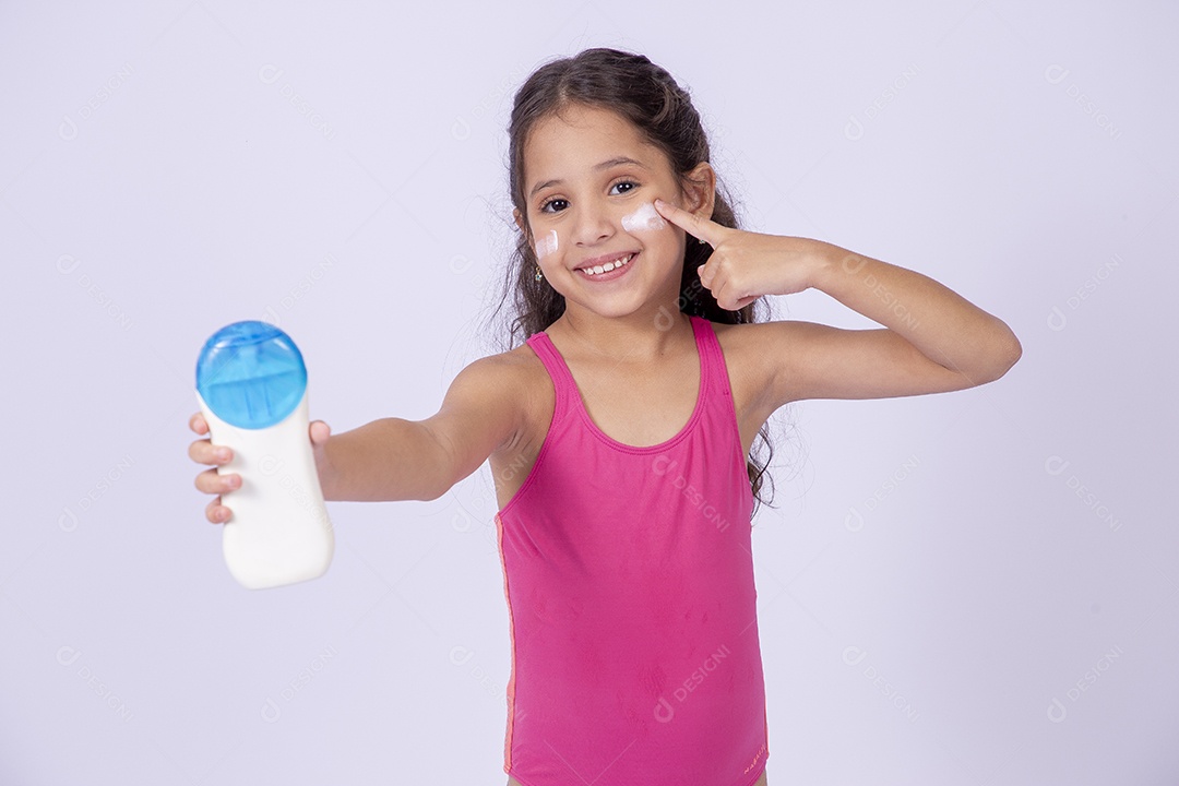 Linda garotinha sorridente com maiô segurando frasco de protetor solar